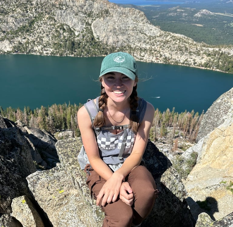 the author sitting on a rock in the mountains. in the background is a lake and a forest of pine.