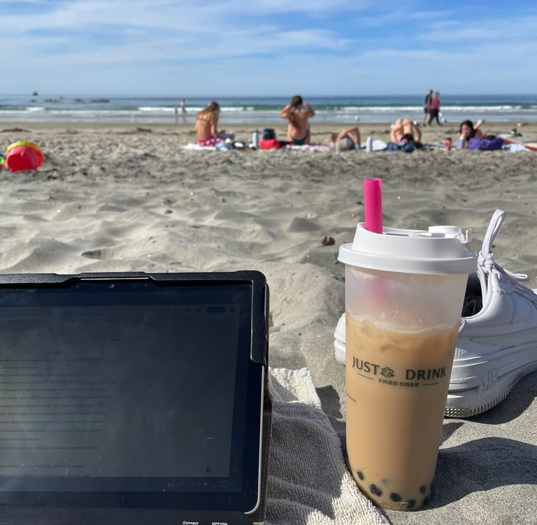 a laptop computer and a cup of brown sugar milk tea with boba sitting on a beach