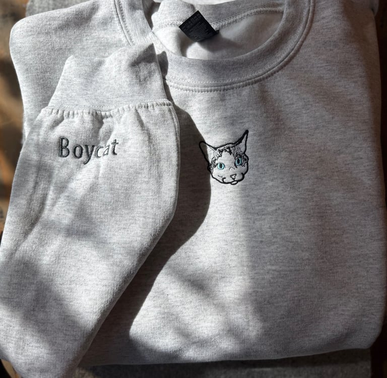 a light gray sweatshirt with a picture of a cat embroidered on it