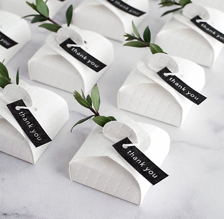 a table with a bunch of small white paper wedding favour boxes