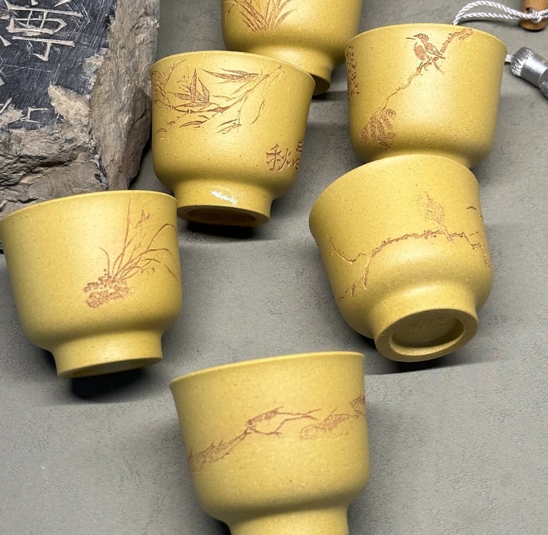 Three yellow teacups engraved with artwork, with an ancient stone beside them