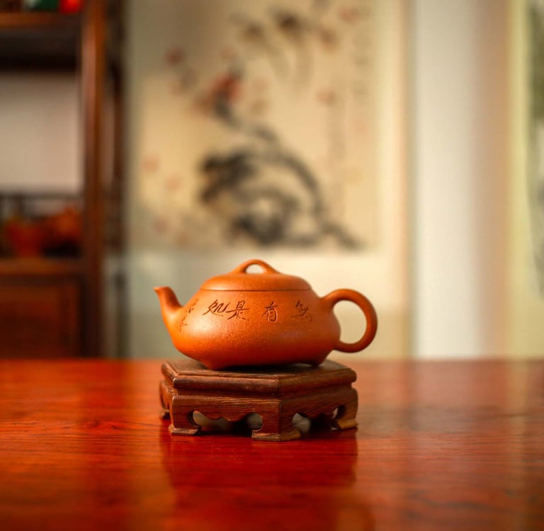A yellow Yixing teapot engraved with Chinese characters is placed on a wooden stand