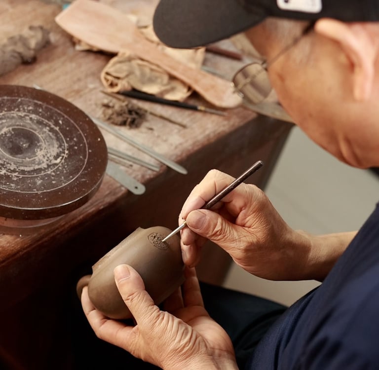 hand holding a tool, making a hole in the body of a teapot