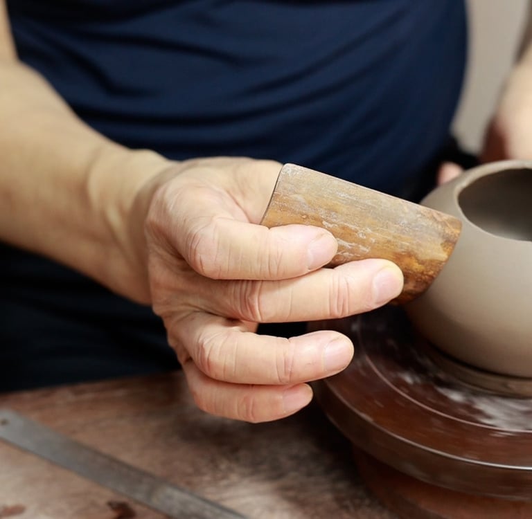 A man using a curved bamboo strip to carefully polish the surface of a Yixing teapot