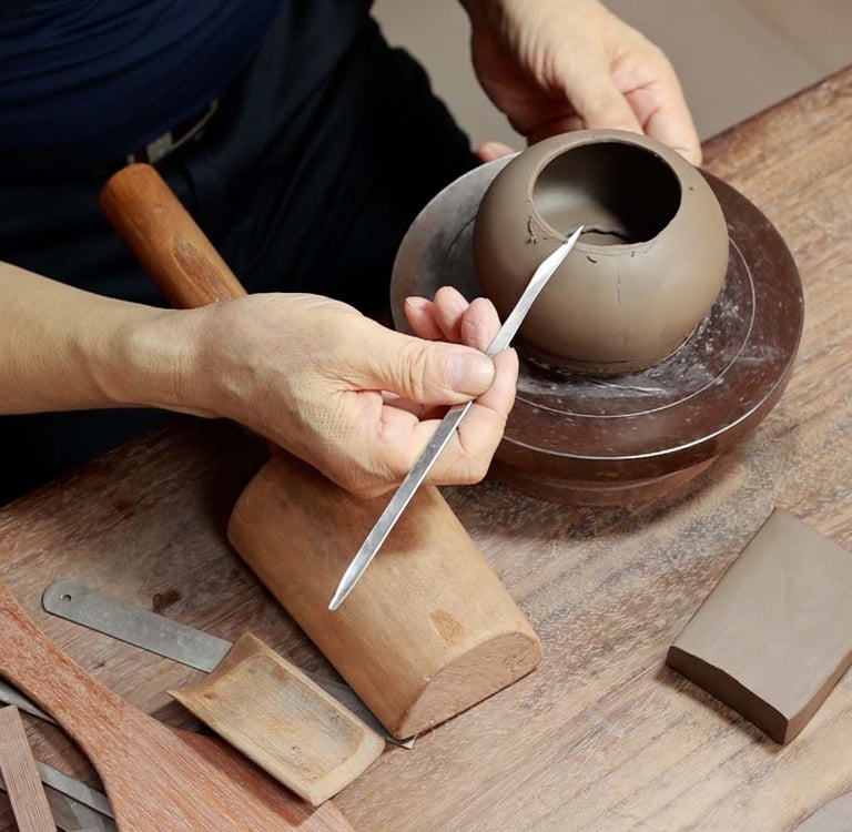 A man holding a long-handled pointed knife, carving the edge of a Yixing teapot