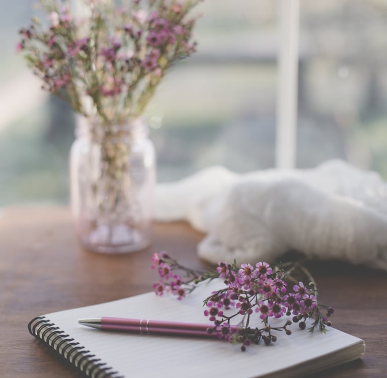 pink pen on spiral notepad with pink flowers nearby