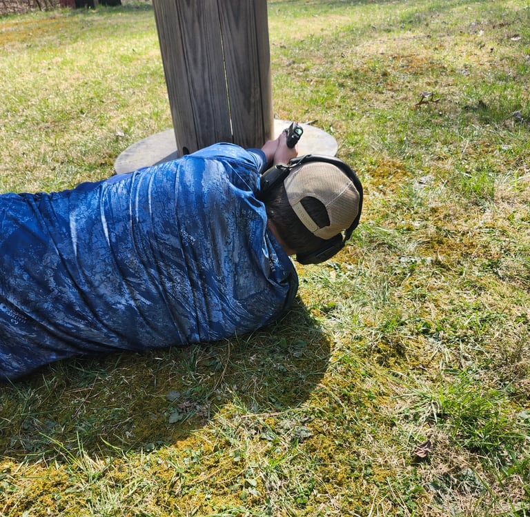 Man laying on side engaging targets from a barrier using self-defense firearm during training.