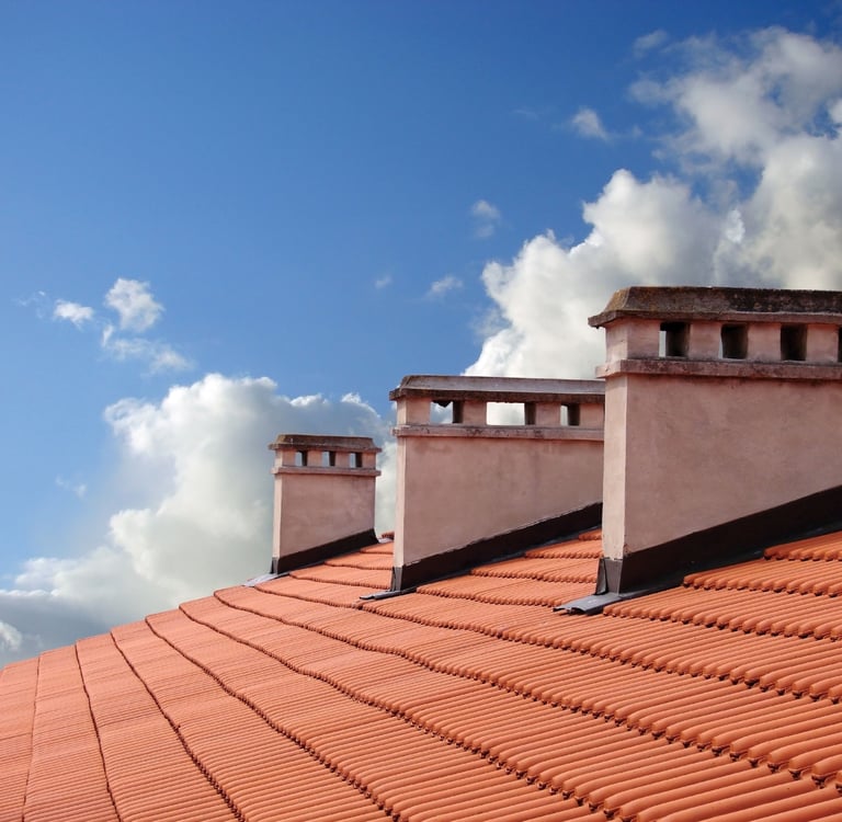 clay roof shingles with 3 white chimneys with a  blue sky background and clouds