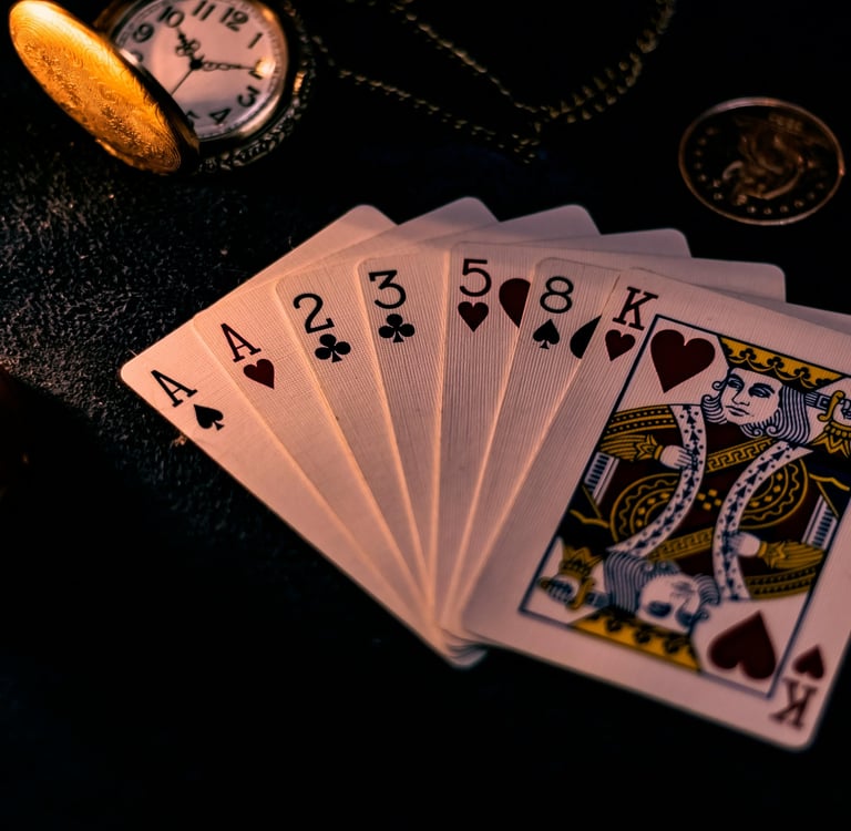 A spread hand of playing cards, witha pocketwatch, coin, chain and candlestick on the same surface in the background.