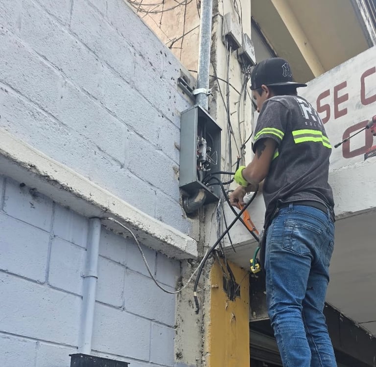 Instalación eléctrica en acometida de edificio por técnico con uniforme.