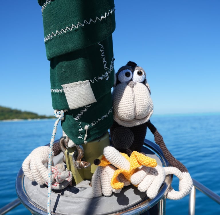 A cute crochet chimpanzee sitting on a sailboat mast with a banana on a sunny day at sea.
