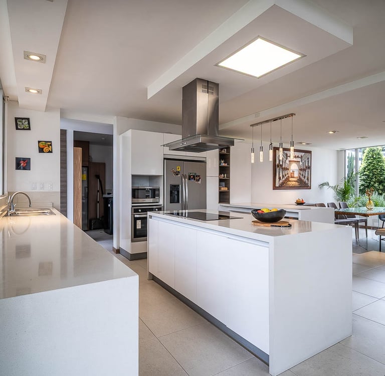 Vista lateral de una cocina estilo americano, paredes blancas y comedor con amplios ventanales