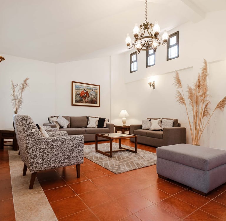 Habitación interior amoblada y decorada con pinturas, candelabro  plantas con sillones cafés AirBnB en Quito, Ecuador
