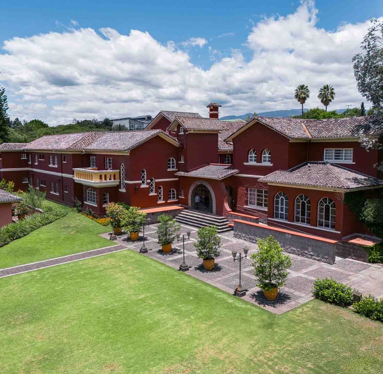 Fotografía aérea de gran casa religiosa de color rojo rodeada de hermoso  jardín verde en Quito Ecuador