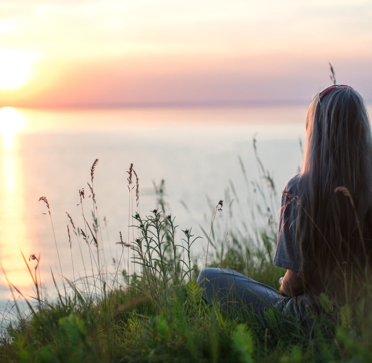 une femme assise dans l'herbe médite face à la mer pour être moins stressée