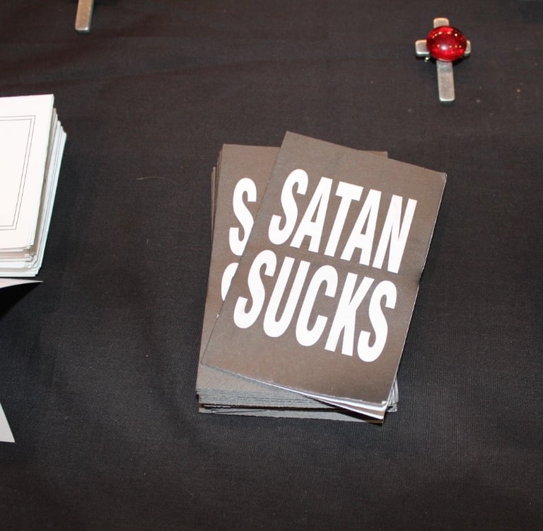 Free handouts at biker ministry table says “Satan Sucks.”