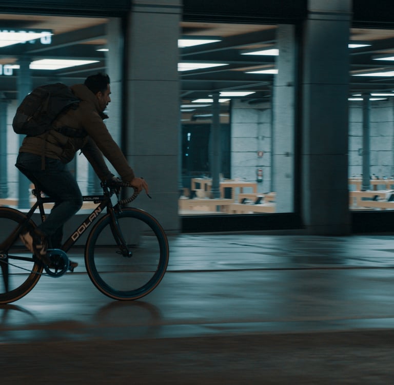 A man on a bicycle rides past a brightly lit shop window at night.