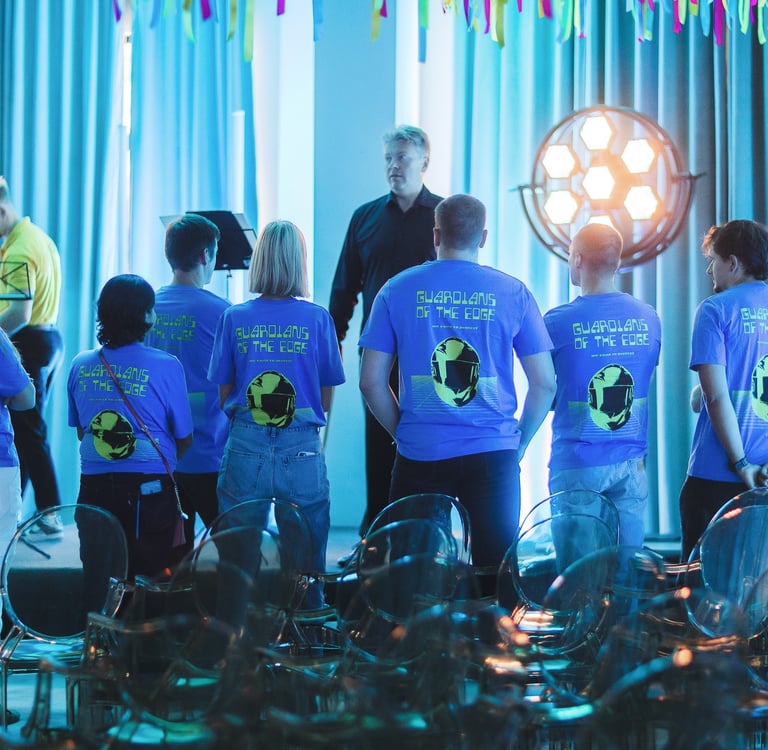 A group of employees in blue corporate t-shirts attending a stage presentation at a tech event.