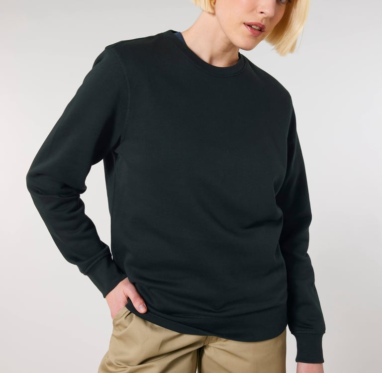 A blonde woman wearing a classic black crewneck sweatshirt and khaki pants against a white background.