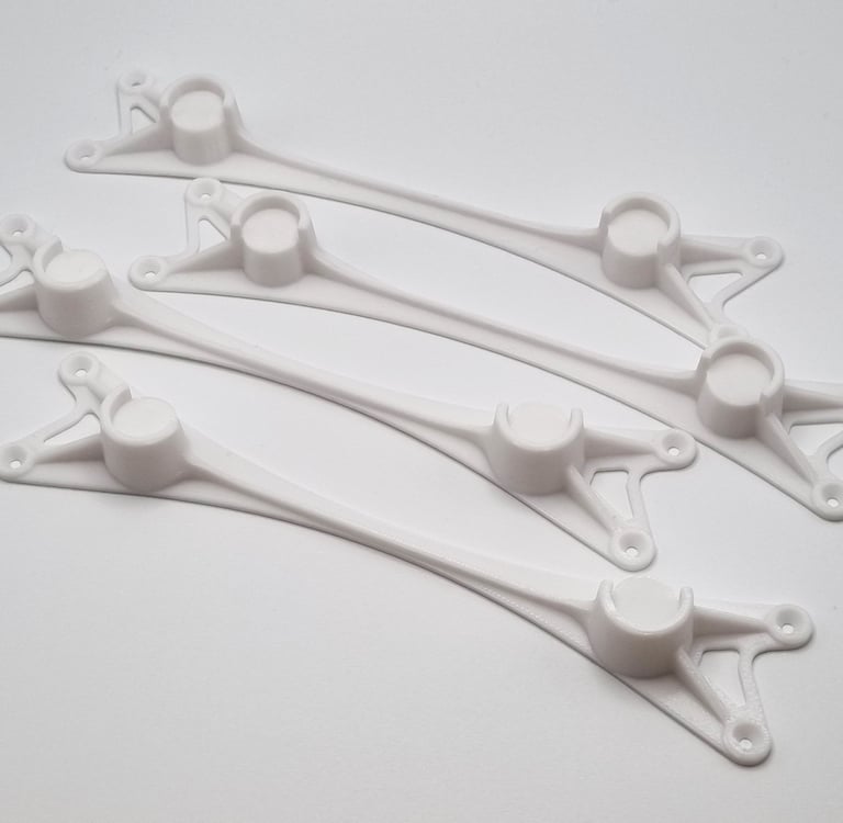 Four white plastic 3D printed drone frame arm replacements arranged on a white surface.