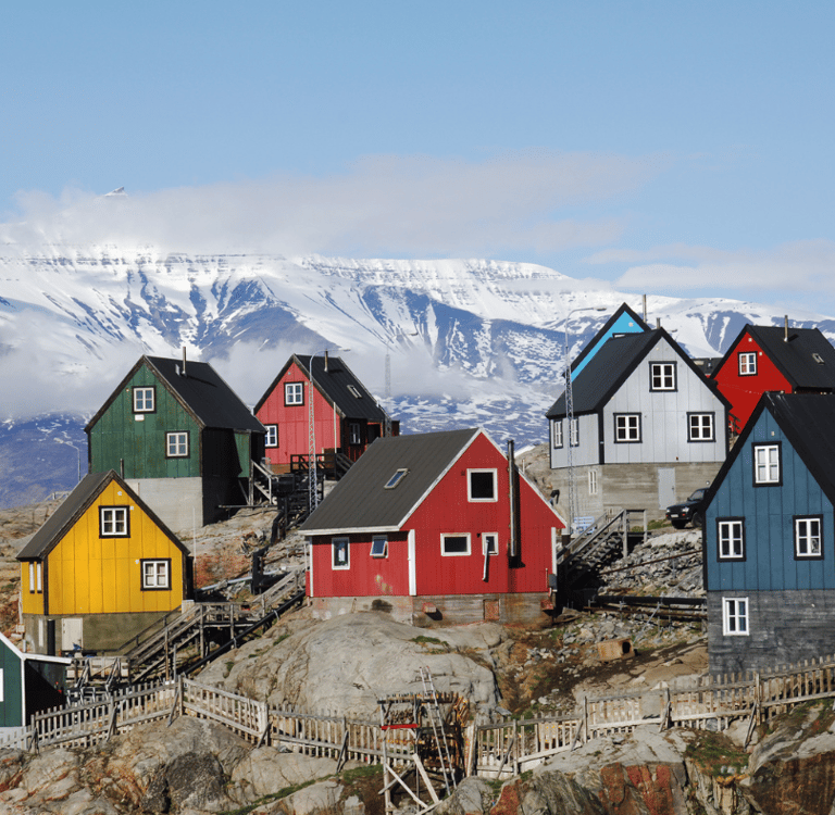 Colorful coastal houses in a Greenland village with snow-capped mountains in the background.