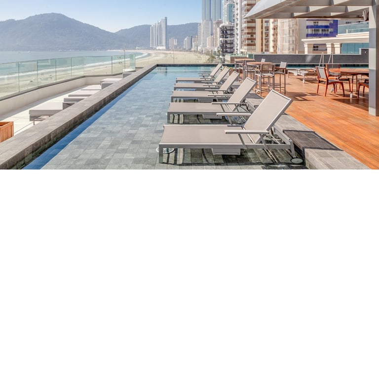 Vista de piscina com cadeiras e a orla de Balneário Camboriú em sua dimensão.