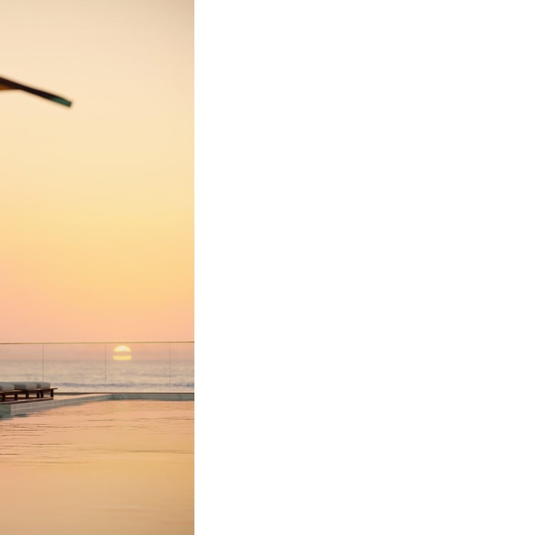 Vista ao nascer do sol, com piscina, cadeiras e guarda-sóis em primeiro plano.