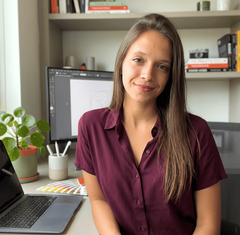 Una diseñadora gráfica sonriente está sentada en su escritorio con una computadora portátil