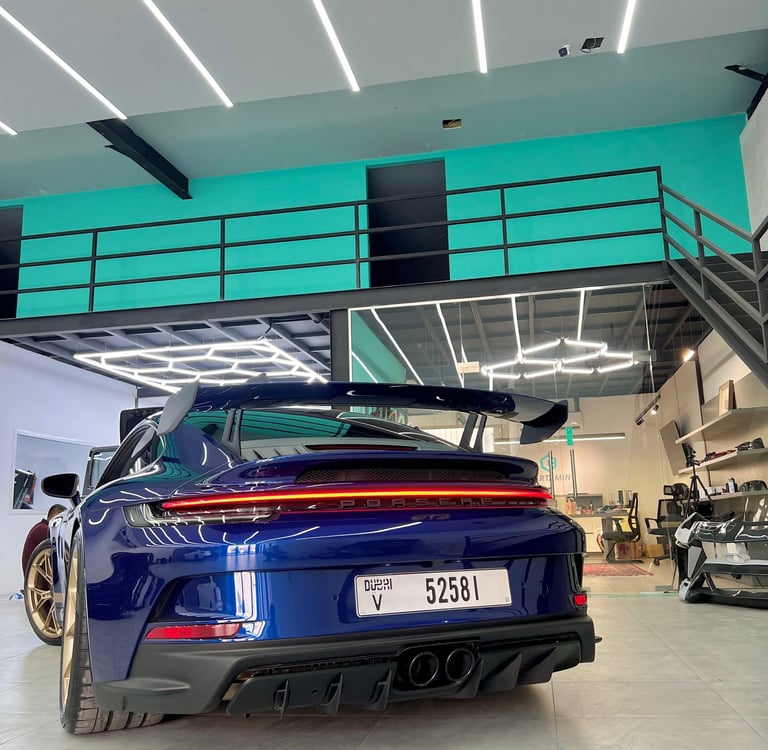 Rear view of a blue Porsche 911 GT3 with a large spoiler in a modern automotive detailing garage.