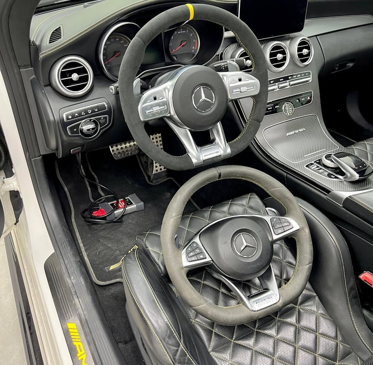 Interior of a Mercedes-Benz AMG featuring Alcantara steering wheels and yellow-stitched leather bucket seats.