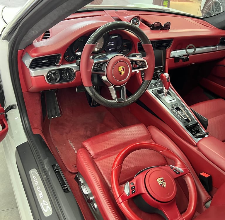 Luxury red leather interior of a white Porsche 911 Carrera 4S with carbon fiber steering wheel.