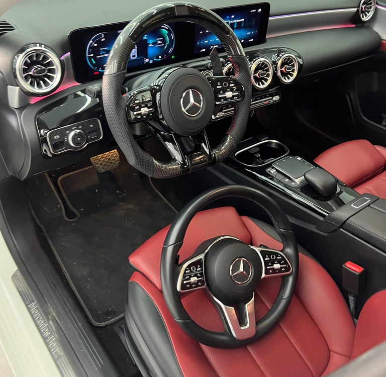 Luxury Mercedes-Benz interior featuring a carbon fiber steering wheel upgrade and red leather seats.