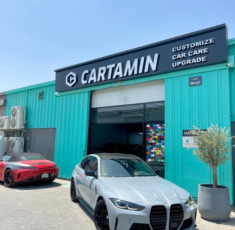 A grey BMW M3 parked outside the Cartamin car care and customization shop in Dubai.