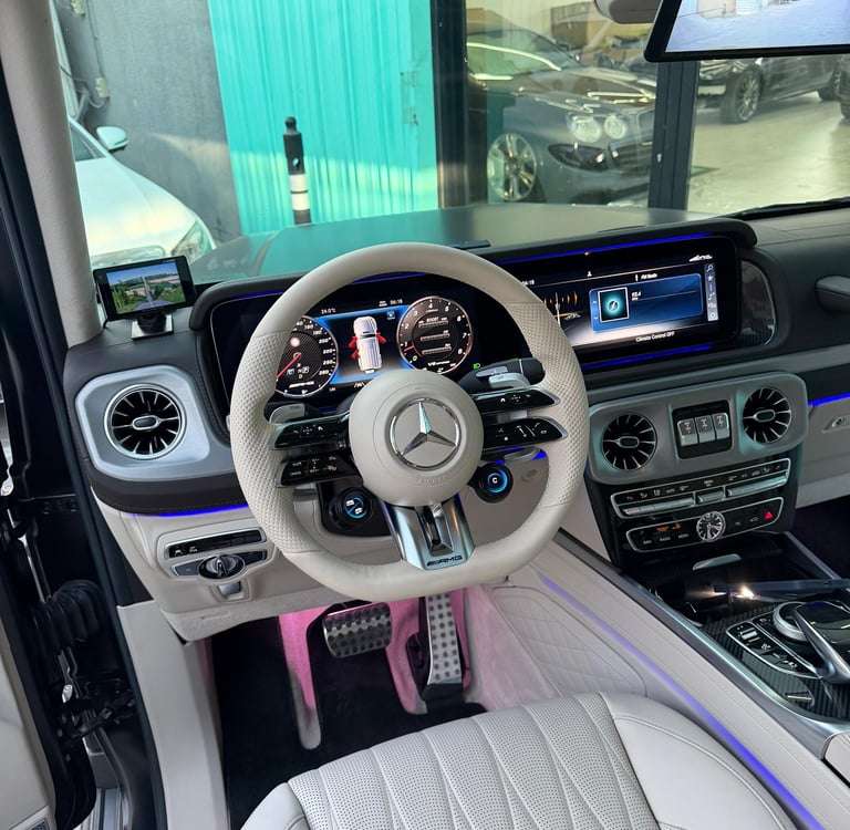 Luxurious Mercedes-Benz AMG G-Wagon interior featuring a white leather steering wheel and digital dashboard.