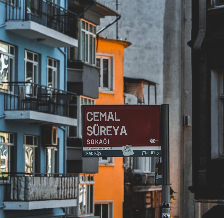 Red Cemal Süreya street sign in the Kadıköy district of Istanbul featuring colorful blue and orange buildings.