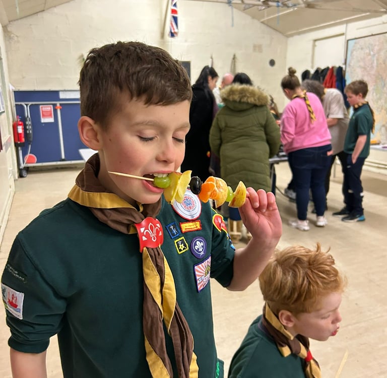 A cub from the 25th Allerton eats some fruit on a stick.