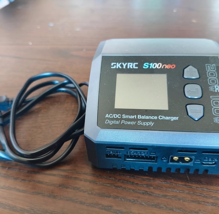 Carregador inteligente SkyRC S100neo AC DC completo com cabo de alimentação elétrica sobre mesa de m