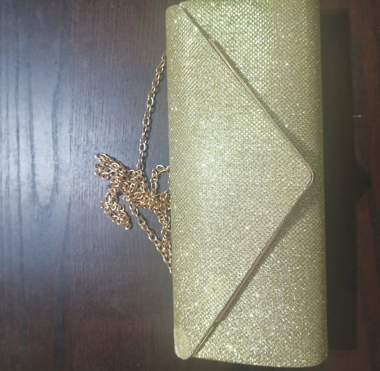 Análise de design de mala clutch dourada estilo envelope com brilho glitter e alça de corrente.
