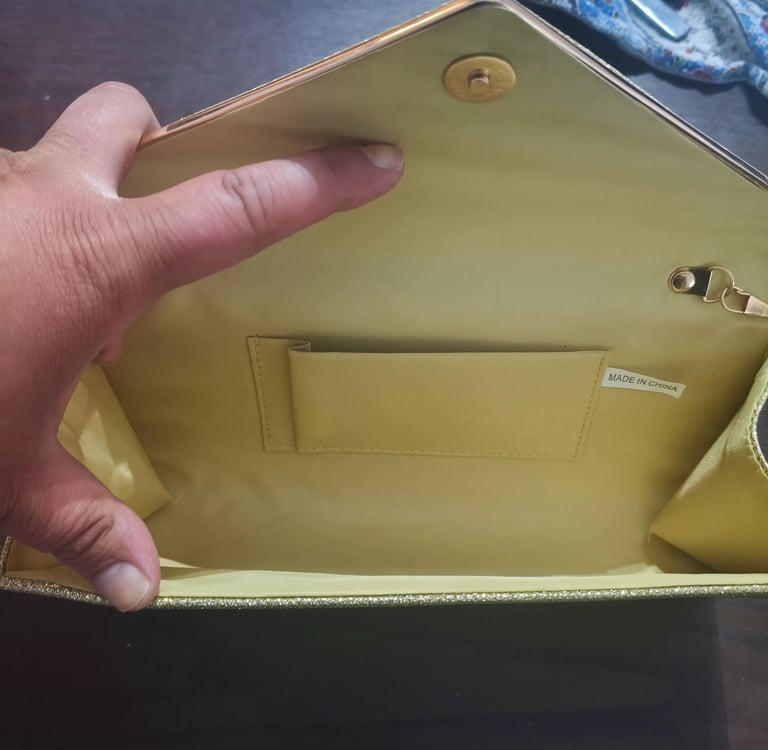 Análise do espaço interior da mala clutch de festa com detalhe do bolso interno para cartões.