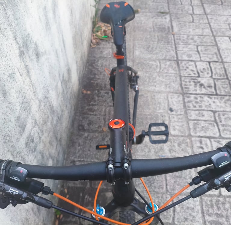 Bicicleta com detalhes a laranja fotografada de cima, junto a parede de pedra
