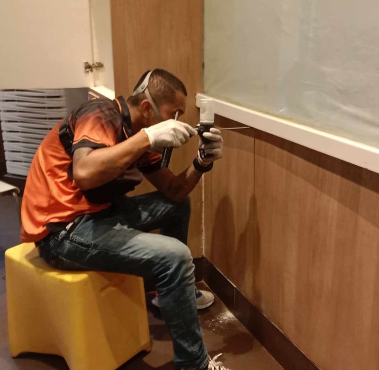 Professional pest control technician inspecting an indoor wall for termites using a specialized tool.