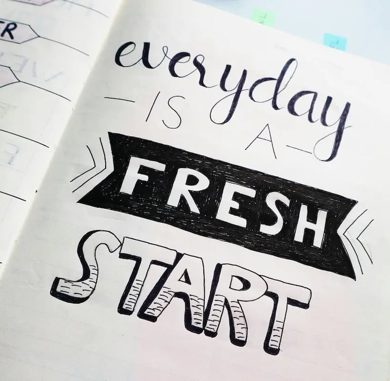 Hand-lettered motivational quote in a bullet journal says everyday is a fresh start with markers nearby.