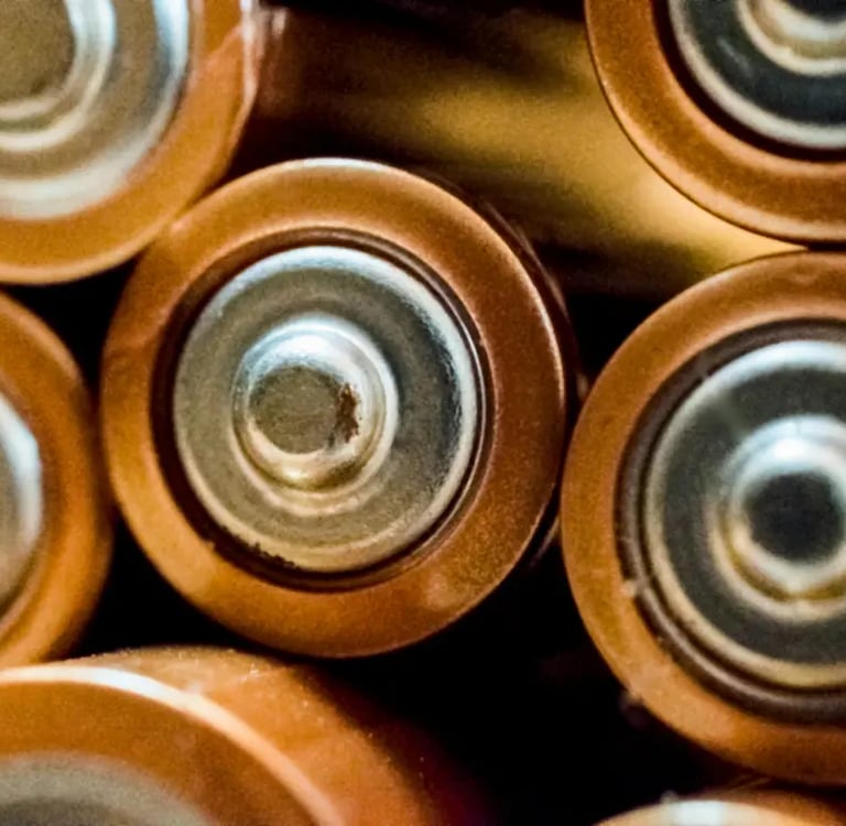 Close-up top view of several copper and gold alkaline AA batteries showing the positive terminals.