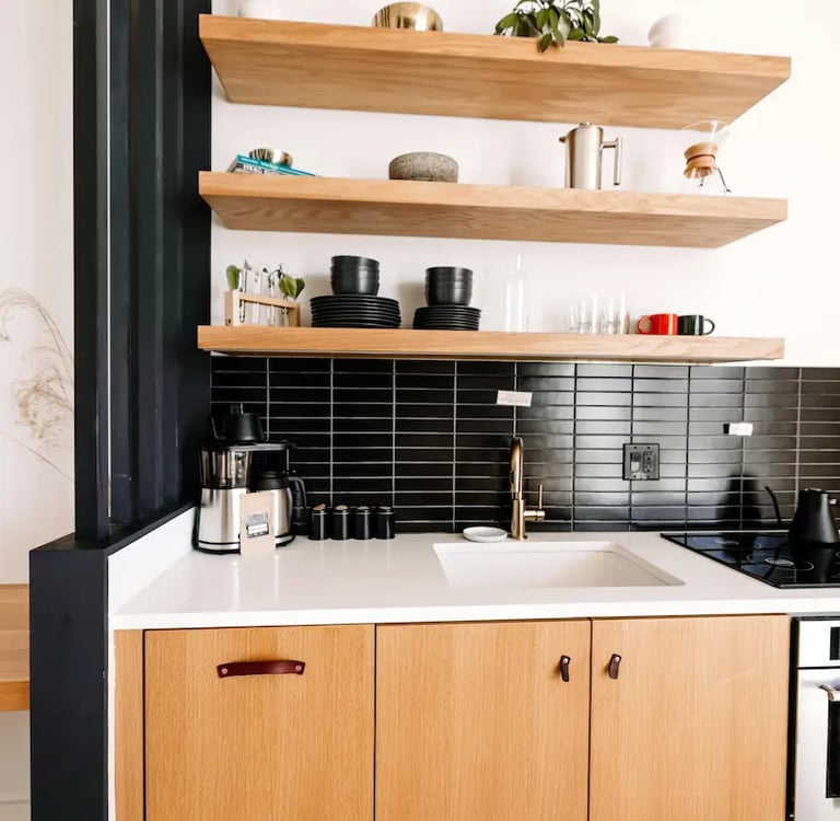 Modern kitchen with natural wood cabinets, floating shelves, and black subway tile backsplash.
