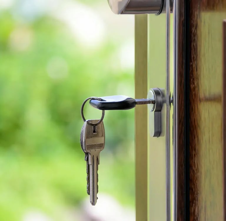 House keys inserted in a wooden door lock with a blurred garden background.