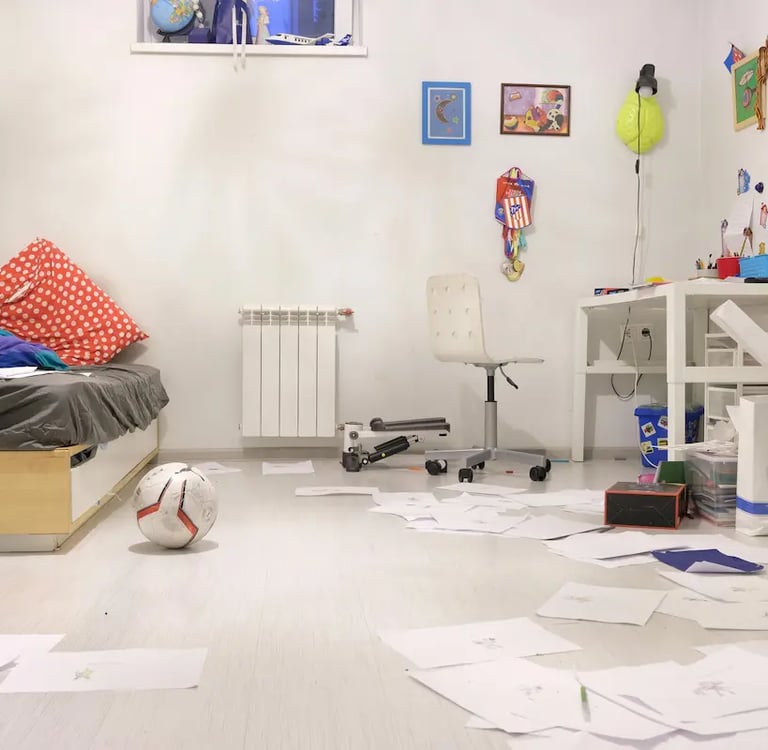 Messy child's bedroom with white walls, scattered drawings on the floor, and a soccer ball.