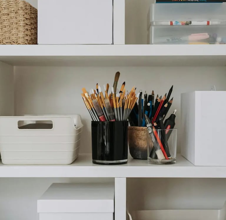Organized art studio white bookshelf featuring paintbrushes, pencils, and craft storage bins.
