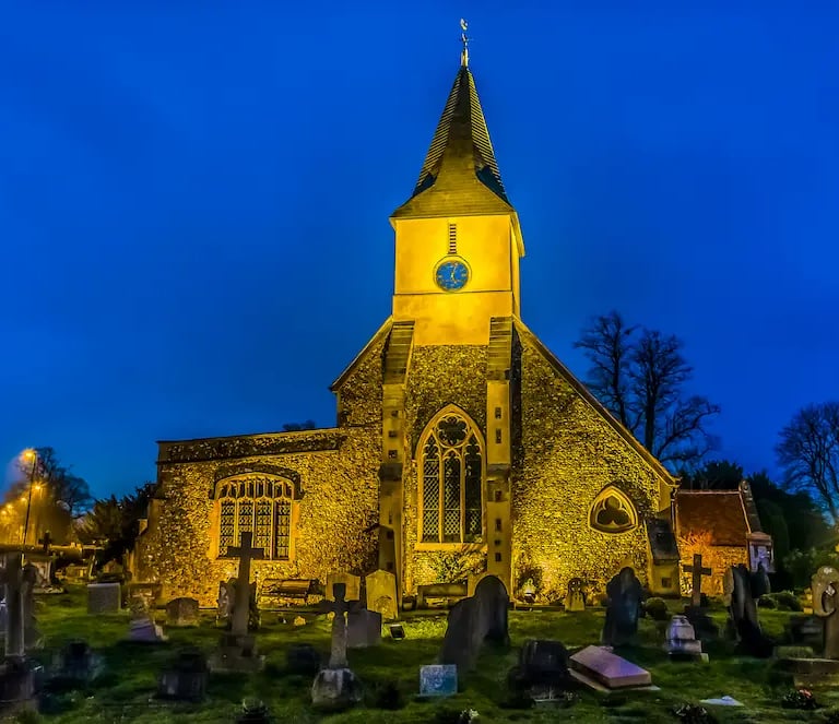 Illuminated historic stone church with a clock tower and cemetery in Sanderstead