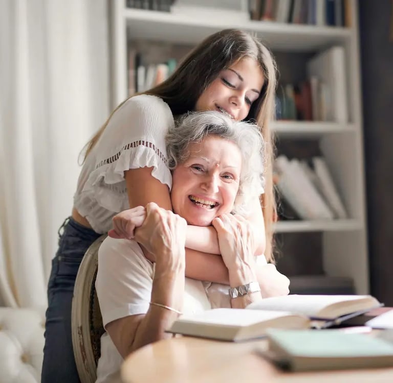 A young woman hugging her happy grandmother at home while reading books together.
