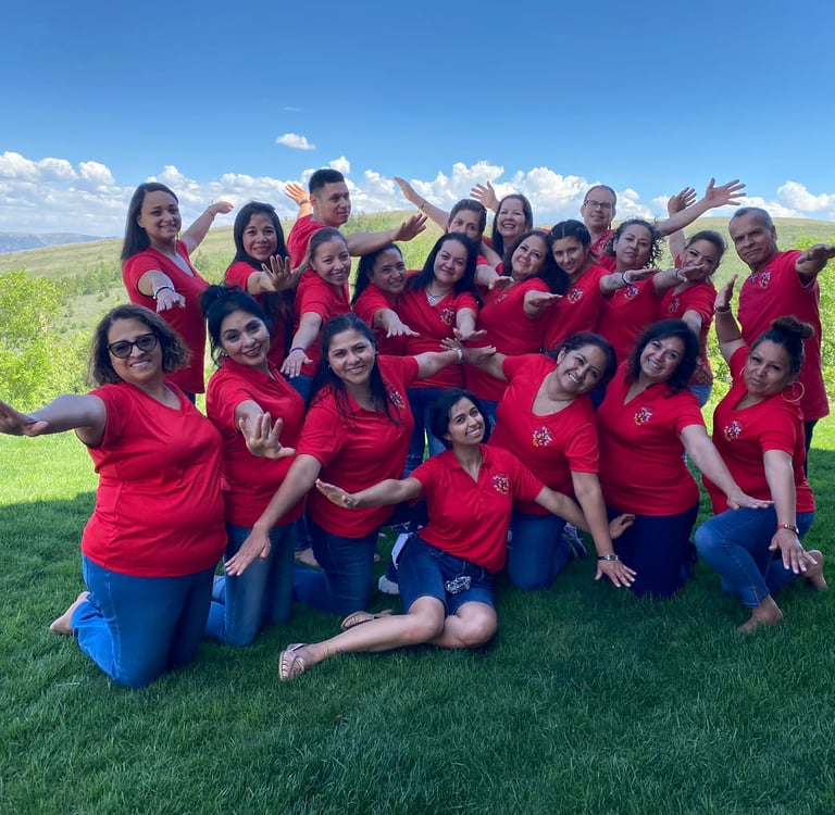 Diverse team of smiling colleagues wearing red shirts posing outdoors on a green lawn.